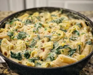 Creamy spinach and artichoke pasta dish garnished with herbs and cheese